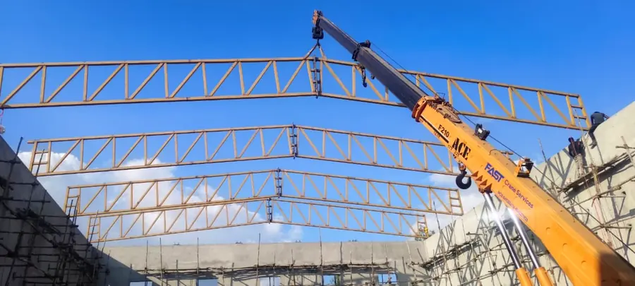 Crane-assisted erection of long-span steel roof trusses at an industrial project.