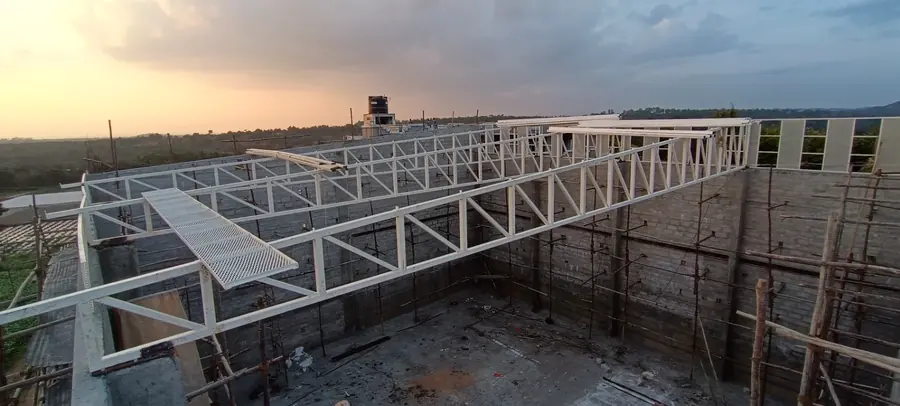White roof truss structure photographed at sunset during erection stage.