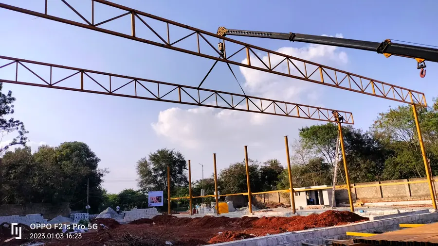 Long steel roof trusses being erected across a wide construction site.